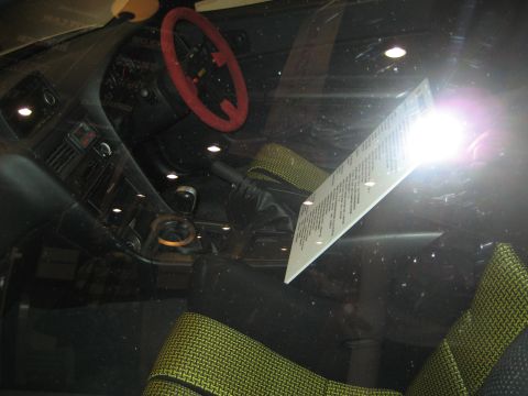 1998 Ford Crown Victoria - The interior of a car shows a red steering wheel, yellow patterned seats, and a document on the dashboard.