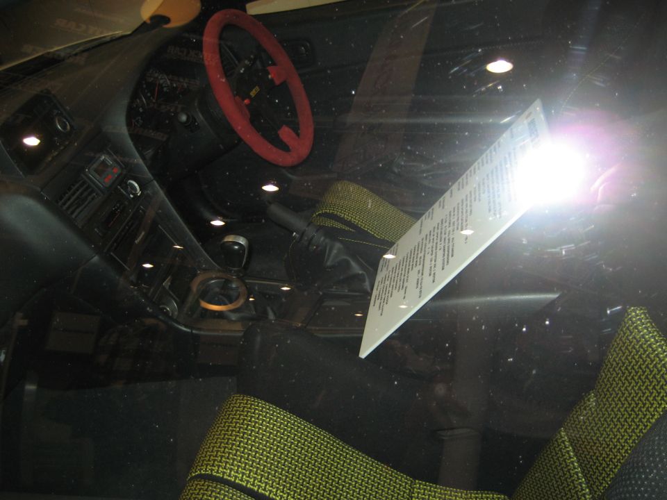 Car interior shot through windshield showing red steering wheel and info card