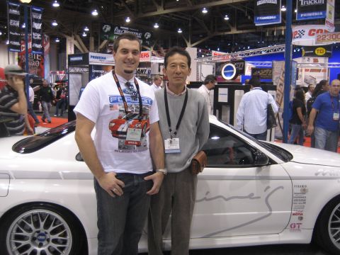 1998 Ford Crown Victoria - Two men pose with a white car adorned with racing decals at an indoor event.
