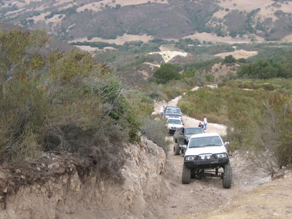White Toyota 4Runner with aftermarket bumper and off-road tires driving on a dirt road