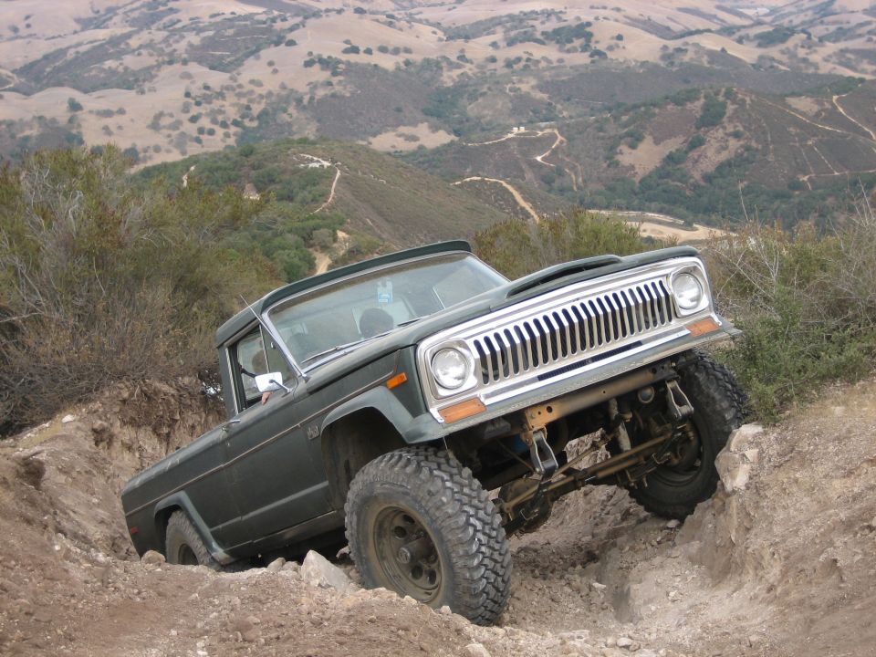 Green off-road pickup truck navigating a steep dirt trail