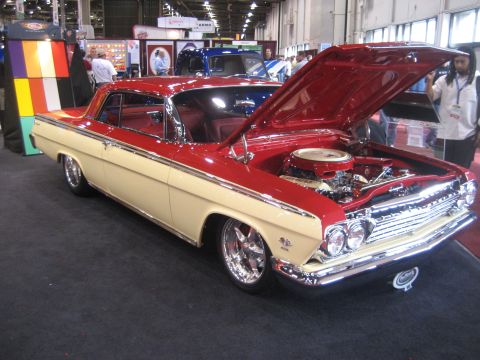 1998 Ford Crown Victoria - A two-tone 1961 Chevrolet Impala coupe is displayed with its hood open, revealing the engine bay.