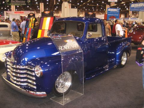 1998 Ford Crown Victoria - Custom blue pickup truck with flame graphics is showcased at an auto show.