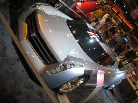 1998 Ford Crown Victoria - A futuristic concept car is displayed indoors with people in the background.