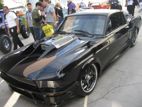 1998 Ford Crown Victoria - A custom black coupe with aggressive styling sits on display, surrounded by onlookers and other vehicles.