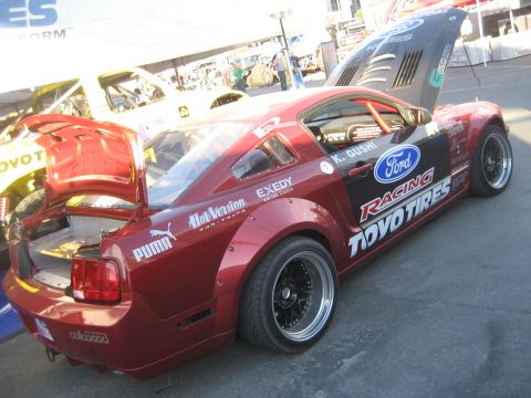 1998 Ford Crown Victoria - A modified Ford Mustang with racing livery and aftermarket wheels is displayed with its hood and trunk open.