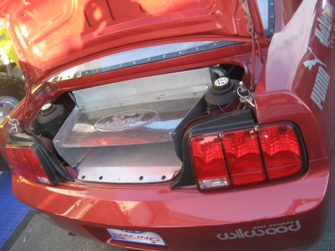 1998 Ford Crown Victoria - The rear of a red car is shown with the trunk open, revealing a Ford emblem and racing stickers.