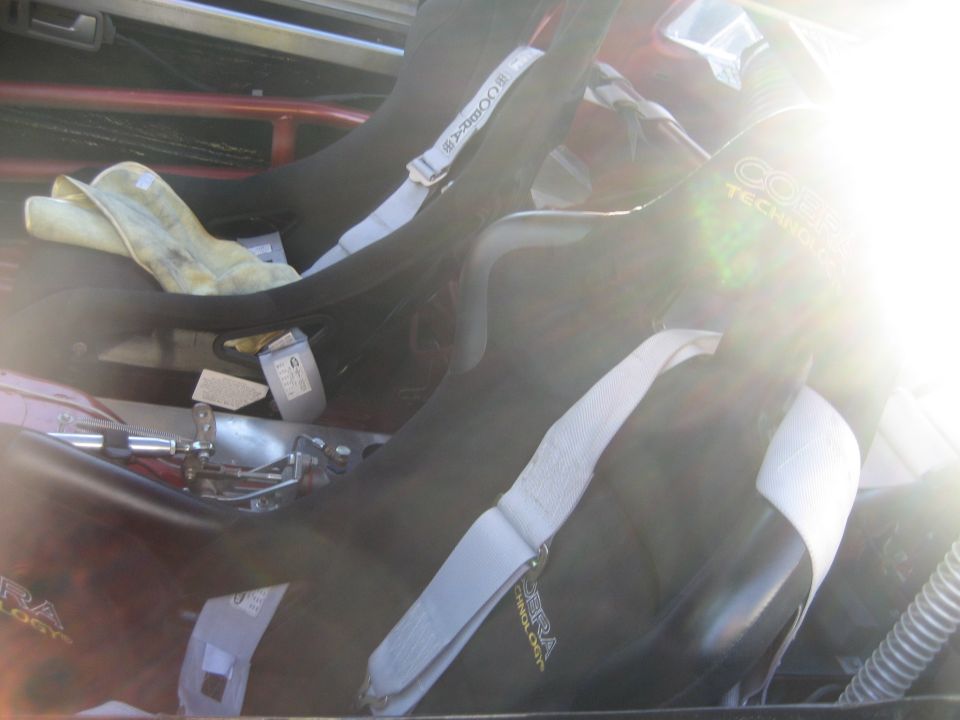 Cobra racing bucket seat with white harness belts in a backlit car interior