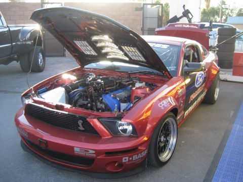 1998 Ford Crown Victoria - This red Ford Mustang has its hood open, revealing the engine bay and various racing decals.
