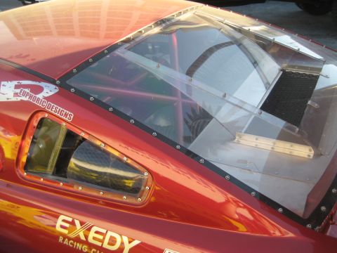 1998 Ford Crown Victoria - A red race car's rear and side windows are modified with clear plastic panels and a visible roll cage.