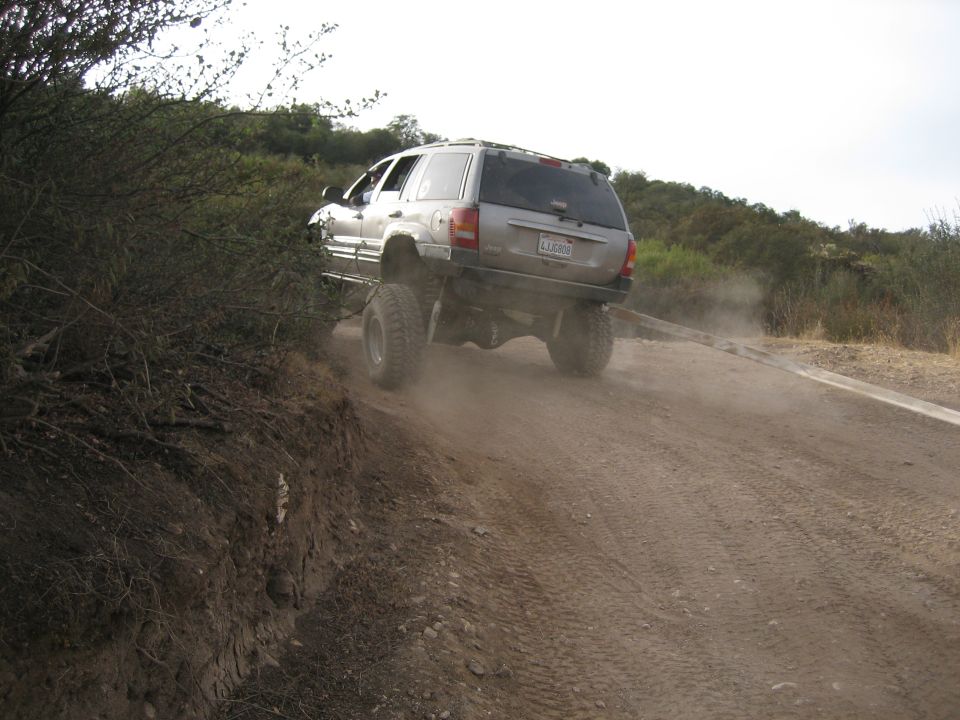 Silver SUV with lifted suspension and large tires driving on a dirt road, kicking up dust