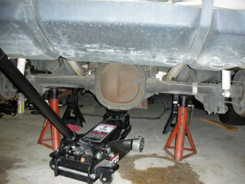 1990 Ford Mustang - The underside of a vehicle is shown with the rear axle assembly raised and supported by safety equipment.