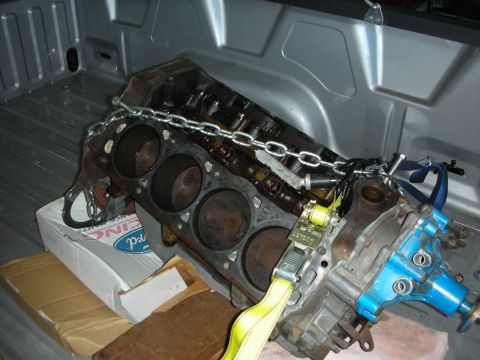 1990 Ford Mustang - A disassembled engine block is being transported in the bed of a pickup truck, secured with chains and straps.