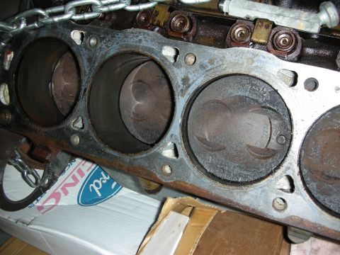 1990 Ford Mustang - Close-up of an engine block's cylinders and pistons, with a partial Ford logo visible on a box underneath.