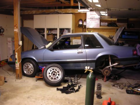 1990 Ford Mustang - 1990 Ford Mustang coupe in a garage with suspension parts laid out for service.