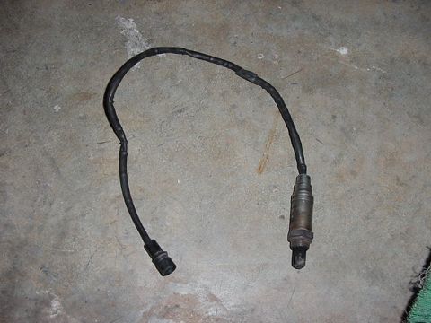 1984 BMW 3 Series - An oxygen sensor with its wiring lies on a concrete surface.