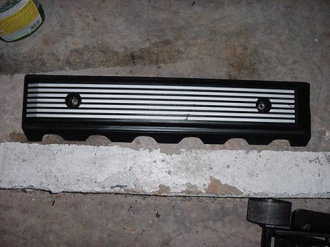 1984 BMW 3 Series - This black engine valve cover features silver horizontal stripes and two visible bolts.