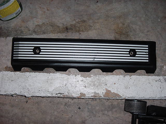Black engine valve cover with silver horizontal stripes and two bolts