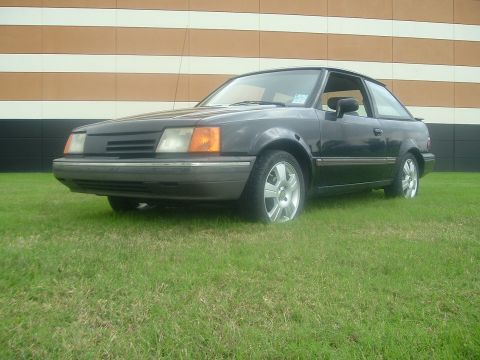 1989 Ford Escort - This 1989 Ford Escort coupe is parked on a grassy area in front of a building.
