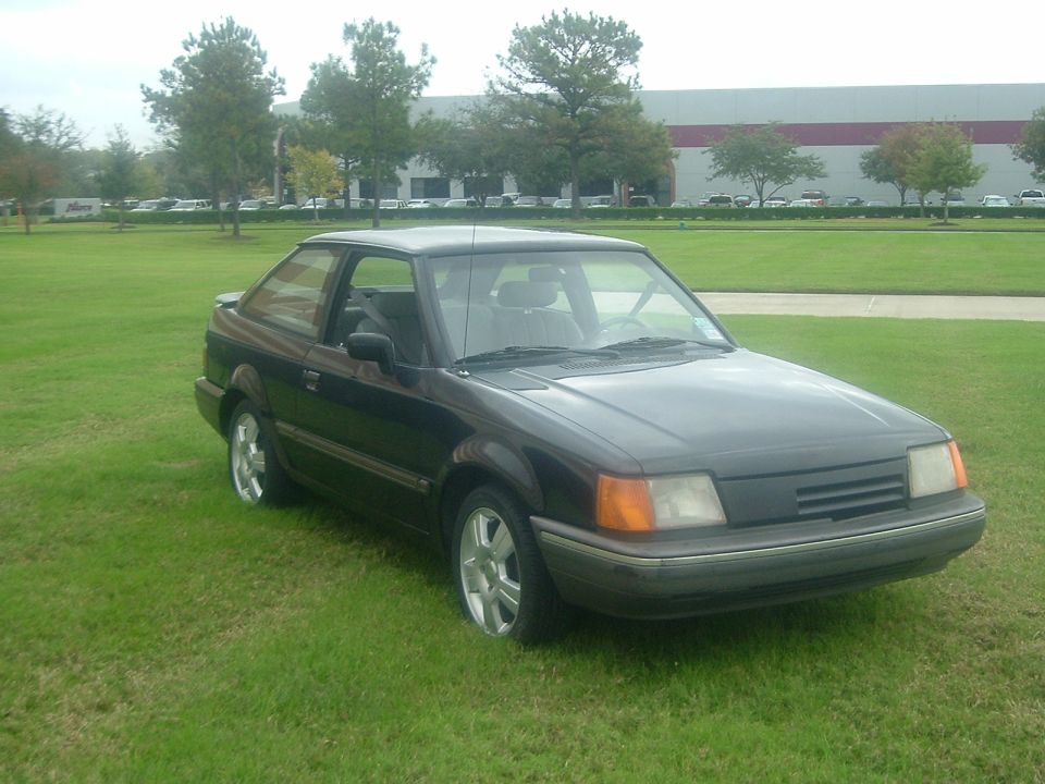 Dark 1989 Ford Escort coupe parked on grass, front 3/4 view