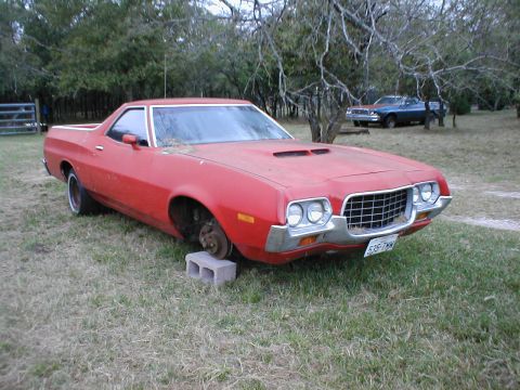 1973 Ford Ranchero - A red 1972 Ford Ranchero sits in a grassy yard with its front wheel removed and replaced by a cinder block.