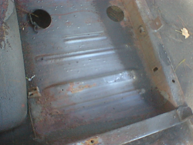Close-up of a stamped sheet-metal floor pan with two round holes and surface rust