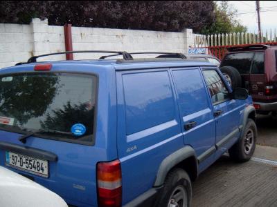 2000 Jeep Cherokee - A blue Jeep Cherokee van, likely a 2000 model, is parked next to another SUV.
