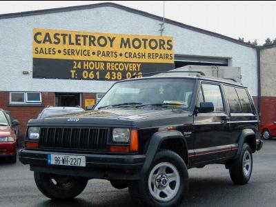 2000 Jeep Cherokee - A black Jeep Cherokee is parked outside a business with a large sign overhead.