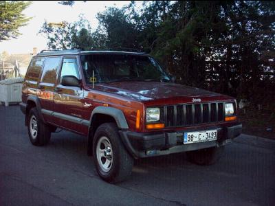 2000 Jeep Cherokee - This Jeep Cherokee XJ is seen from the front quarter angle on a paved road with trees in the background.