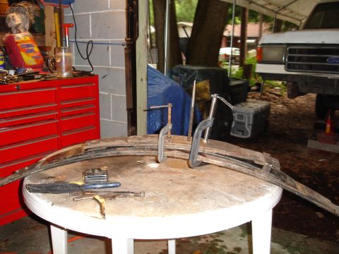 1989 Ford Bronco - A leaf spring is being worked on in a garage setting, with a white Ford truck visible in the background.
