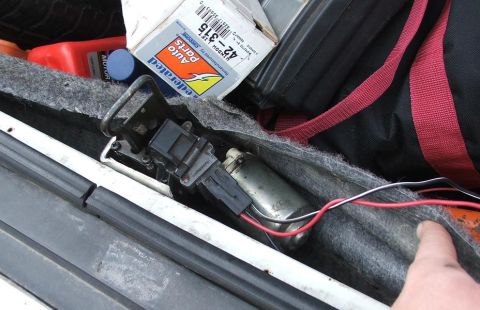 1985 Ford Crown Victoria LTD - Close-up view of a power trunk actuator mechanism, alongside a box of auto parts and other items stored in the trunk.