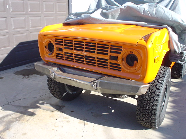 1977 Ford Bronco front end with orange paint, custom bumper, and cover on hood