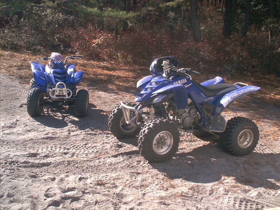Two blue Yamaha ATVs parked on sandy trail in wooded area