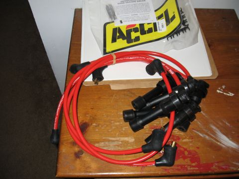 1991 Mitsubishi 3000GT - A set of red Accel spark plug wires and their packaging are displayed on a wooden table.