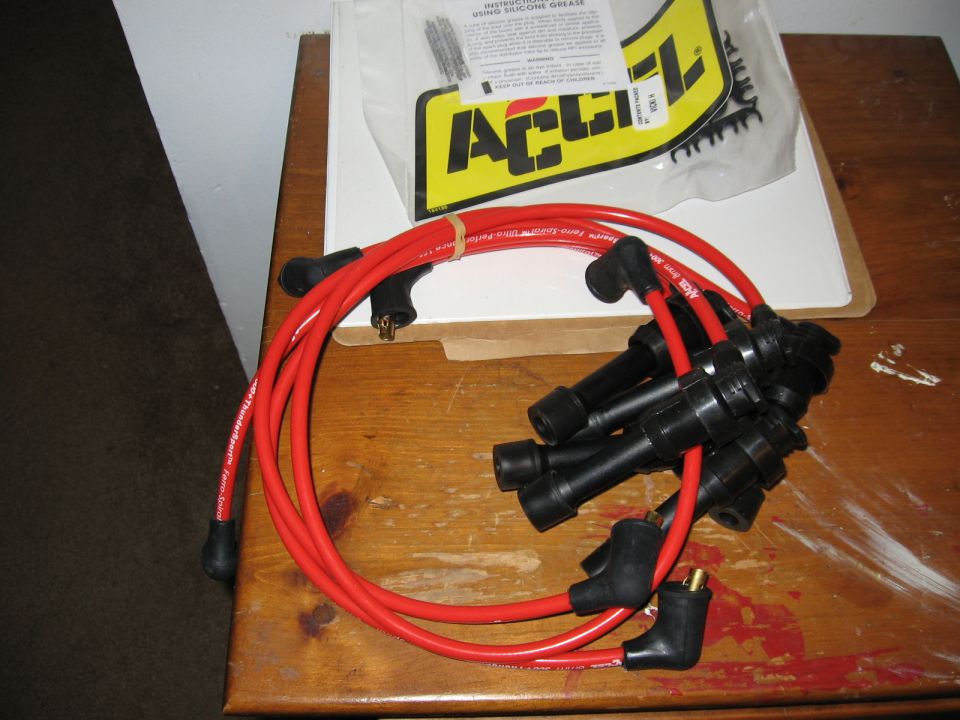 Red ACCEL spark plug wire set with black boots on wooden table with packaging
