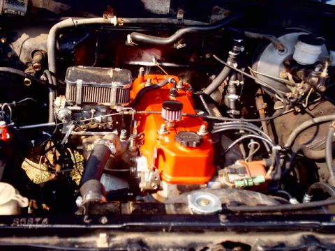 1988 Toyota 4Runner - Close-up view of a vehicle's engine bay, an orange-painted valve cover and a chrome air filter housing.