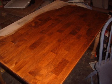 1988 Ford Bronco - A dining table is shown in the process of being refinished, with stain applied to a portion of its surface.
