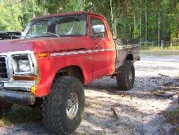 1974 Ford F-100 - This red pickup truck is parked outdoors on a dirt lot with trees in the background.