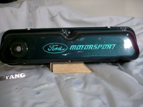 1965 Ford Mustang - A green Ford Motorsport valve cover is shown, with the word "Mustang" visible on a separate emblem in the foreground.
