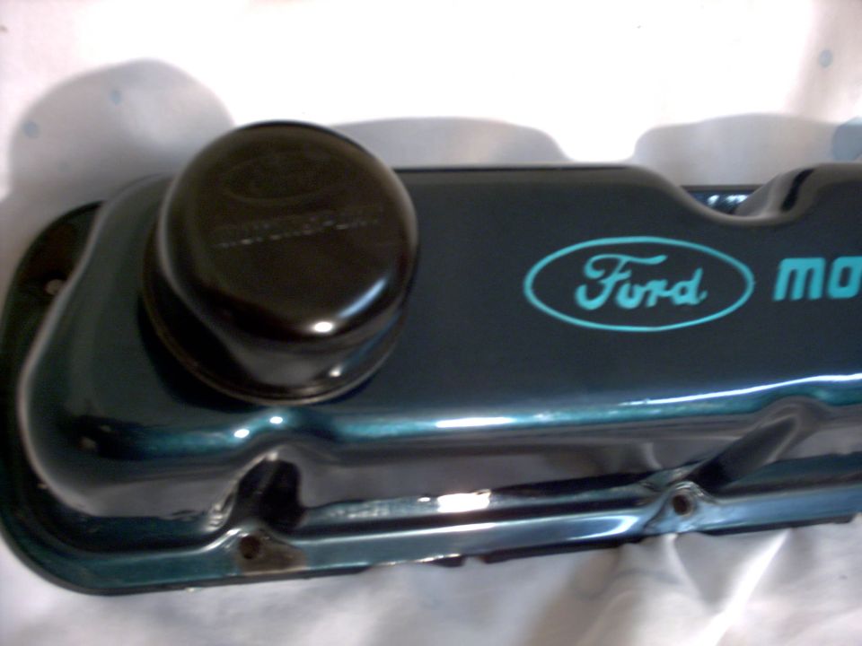 Dark teal Ford valve cover with blue oval Ford logo and 'motor' text. Black oil cap on top