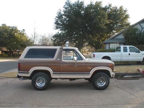1988 Ford Bronco - This two-tone brown and tan SUV is parked on a residential street next to a white pickup truck.