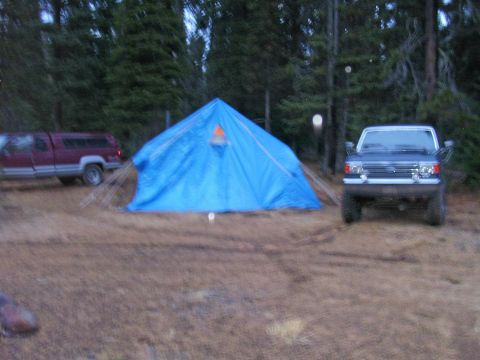 1991 Ford Bronco - A campsite scene a blue tent, a Ford Bronco, and a red pickup truck in a wooded area.