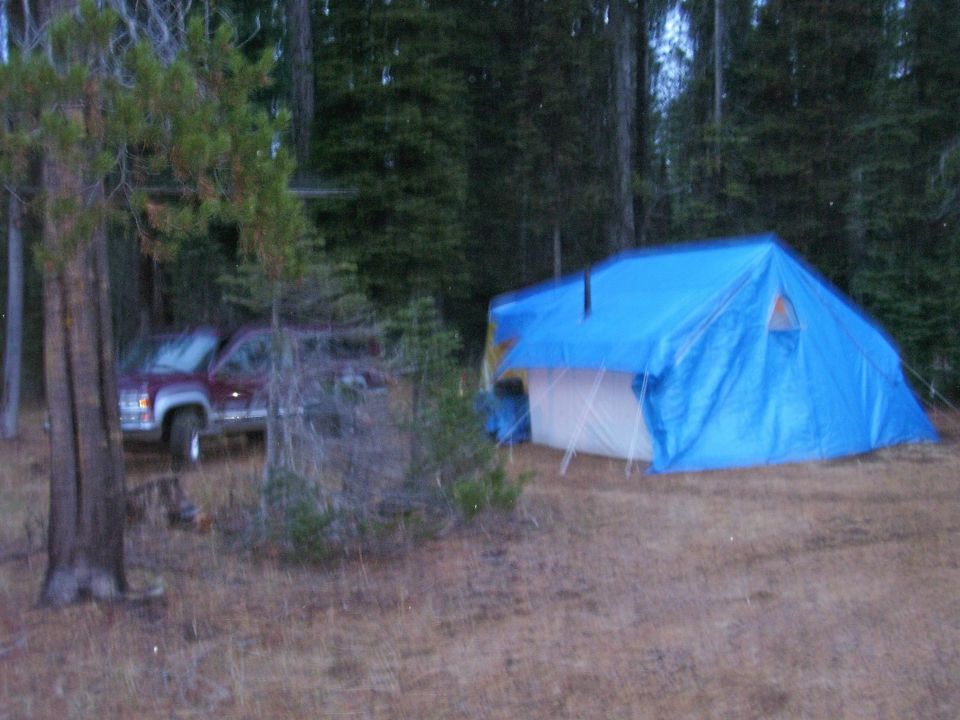 Maroon pickup truck parked in a wooded area next to a blue tent