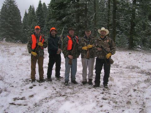 1991 Ford Bronco - Five hunters pose with rifles in a snowy forest, dressed in camouflage and orange safety vests.