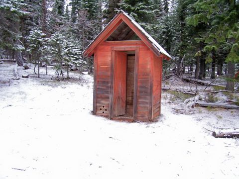 1991 Ford Bronco - An old red outhouse stands in a snow-covered forest clearing, its door ajar.