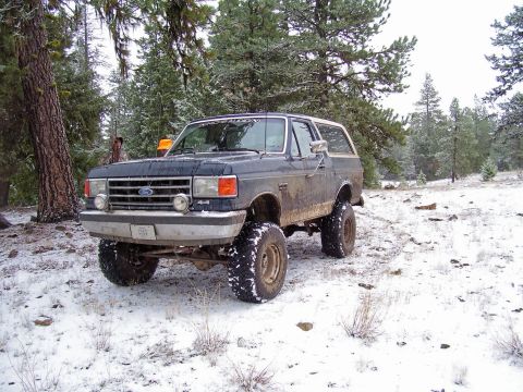 1991 Ford Bronco - Lifted 1991 Ford Bronco navigates a snowy, wooded terrain.