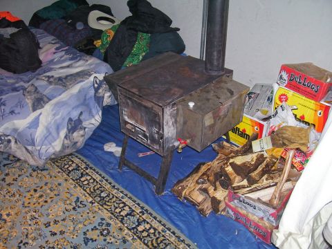 1991 Ford Bronco - A wood stove sits on a blue tarp, surrounded by camping gear and fuel supplies.