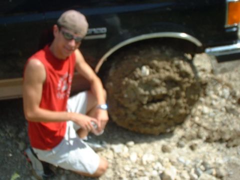 1988 Ford Bronco - A man inspects the mud-covered tire of a 1988 Ford Bronco after an off-road incident.