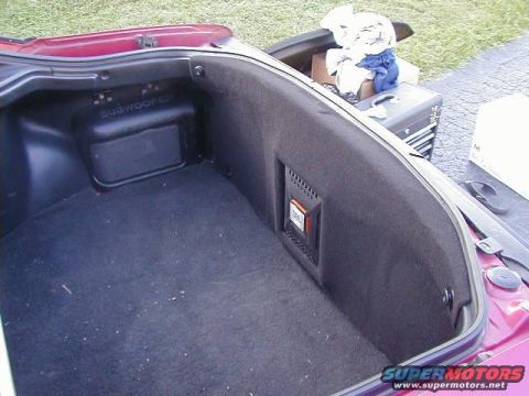 1993 Ford Probe - Open rear hatch of a dark red hatchback showing a black-carpeted cargo area with a factory enclosure embossed SUBWOOFER on the forward pane…