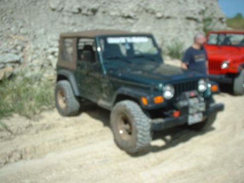 1988 Ford Bronco - Two Jeep Wranglers are parked on a dirt road with a rocky hillside in the background.